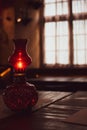 Small oil lamp on the table. Old oil lantern with window on background. Red kerosene lamp. Cozy rustic interior. Evening concept. Royalty Free Stock Photo