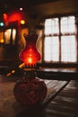 Small oil lamp on the table. Old oil lantern with window on background. Red kerosene lamp. Cozy rustic interior. Evening concept. Royalty Free Stock Photo