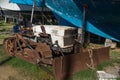 A small old abandoned bulldozer is rusting in a yacht yard