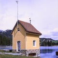 A small old colorful wooden cabin on a dam in the Alps in Spring, shot with analogue film slide technique