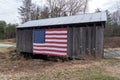 Small old desolated rural wooden house in the wooded area with a flag of USA on the entrance