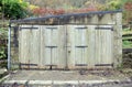 Small old stone storage or garage building with decaying wooden doors and rusted hinges with damp walls and roof