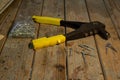 A small old tool rivet with yellow handles lies on a wooden table. Nearby are rivets in a bag and on the table. Low key