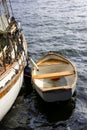 Small old wooden rowing boat moored with rope to a historical white sailboat as a rescue boat for nautical concept, Royalty Free Stock Photo