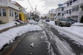 Small one way snow covered street with the center partially plowed and cars parked on both sides in deep snow