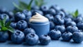 A small, open container filled with creamy substance is surrounded by fresh blueberries on a blue surface. Royalty Free Stock Photo