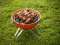 Small orange barbecue on a grass in a park with marinated beef on metal skewers. Selective focus. Concept cooking food outdoors