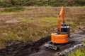 Small orange color mini digger working in a field with a wide bucket. Heavy machinery equipment. Construction industry