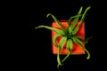 Small orange cute gift box with green cananga flower decoration on black background. Copy space for your text or design.
