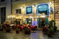 Small outdoor restaurant on cobblestone street illuminated in the evening in Rome
