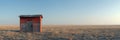 A small outhouse stands alone in the middle of a vast, golden wheat field under a clear blue sky on a sunny day Royalty Free Stock Photo