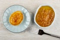 Small pancake with lemon jam in saucer, lemon jam in bowl, fork on wooden table. Top view