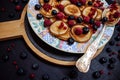 Small pancakes with berries on a patterned plate with silver spoon in rustic style. Traditional breakfast on black table Royalty Free Stock Photo