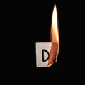 Small paper with letter D burning on a black background