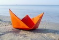 Small paper orange boat on sand near water on background of sea waves Royalty Free Stock Photo