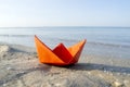 Small paper orange boat on sand near water on background of sea waves Royalty Free Stock Photo