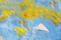 A small paper plane flies over a blurred abstract geographical map of the world. Royalty Free Stock Photo