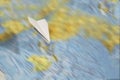 A small paper plane flies over a blurred abstract geographical map of the world. Royalty Free Stock Photo