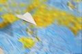 A small paper plane flies over a blurred abstract geographical map of the world.