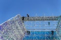 Small part of big high building construction with silhouettes of workers, geometric structure, steel frame. Modern Royalty Free Stock Photo