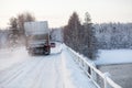 Small passenger car and lorry driving on bridge across a river on snowy road at winter season