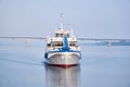 Small passenger motorship on the river and road bridge in the morning haze in the background