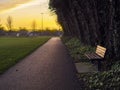 Small pathway in a park and one empty bench, sunset sky in the background. Nobody. Calm relaxing scene