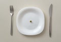 A small pea on a white plate on a white table with a knife and fork, minimum calories Royalty Free Stock Photo