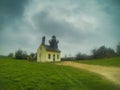 Small picturesque lighthouse on a hilltop by the sea with a dirt road leading up to it under a dramatic grey sky, in