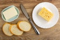 Piece of butter in spotted plate, table knife, piece of cheese in plate, slices of bread on wooden table. Top view Royalty Free Stock Photo