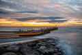 Small pier extending into silky smooth ocean at sunset.