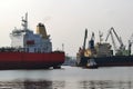 A small pilot ship leads a large red cargo ship at the seaport on a windless autumn day
