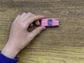 A small pink car in a boy`s hand on a wooden table. Close-up. Copy space. Car buy, sell, rent concept.