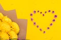 Small pink chrysanthemums in the shape of a heart and a large bouquet of lush flowers on bright yellow background with copy space