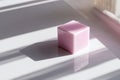 Small pink solid cube casting intricate shadows and reflections on a glossy white surface in soft natural sunlight by a window Royalty Free Stock Photo