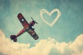 A small plane is seen soaring through the sky with a heart-shaped design painted on its exterior, A vintage airplane skywriting a Royalty Free Stock Photo