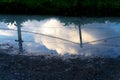 Small plash with the reflection of cloudy sky and metal poles with a chain