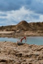 Small plastic toy excavator with bucket working on sand extraction at quarry. Pond in background. Children`s toy model of tractor Royalty Free Stock Photo