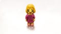 A small plasticine figure of a baby doll in a pink sweater and with yellow hair on a white background