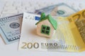 Small plasticine white toy house with green roof stands on the banknotes of dollar and euro lying on laptop. Royalty Free Stock Photo