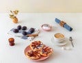 Plate with plum tarts with cinnamon and icing sugar on white wooden table, tasty puff pastry dessert.