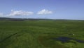 Small pond in the middle of dry green grass. Clip. Aerial of autumn countryside landscape. Royalty Free Stock Photo