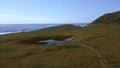 Small pond in the middle of dry green grass. Clip. Aerial of autumn countryside landscape and the sea shore. Royalty Free Stock Photo