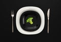 A small portion of boiled broccoli on a black and white plate with a knife and fork on a black table, minimum calories