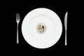 Small portion of tagliatelle pasta on round white plate with fork and knife on isolated black background.