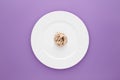 Small portion of tagliatelle pasta on round white plate on light purple background.