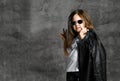 Small positive girl in black and white rock style casual clothing and sunglasses standing and feeling happy with raised hand Royalty Free Stock Photo