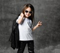 Small positive girl in black and white rock style casual clothing and sunglasses standing and feeling happy with raised hand Royalty Free Stock Photo