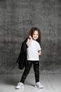 Small positive girl in black and white rock style clothing and white sneakers standing and posing over grey concrete background Royalty Free Stock Photo