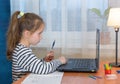 Small preschooler girl in headphones sit at desk study online on laptop smart little kid wear earphones handwrite in notebook